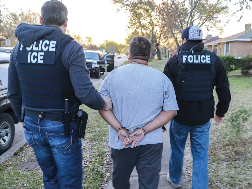 Agentes del Servicio de Inmigración y Control de Aduanas (ICE) escoltan a un hombre durante una operación.